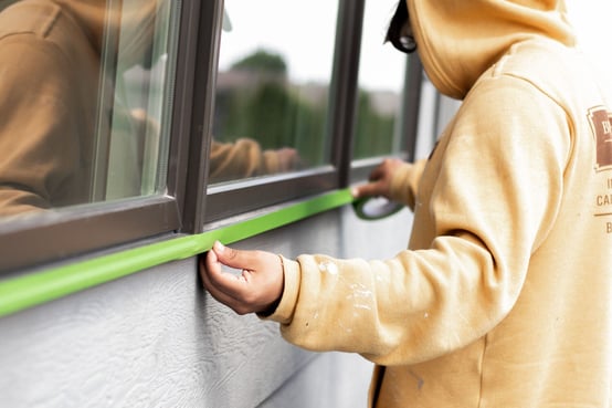 Painter taping off windows of exterior of home before painting.