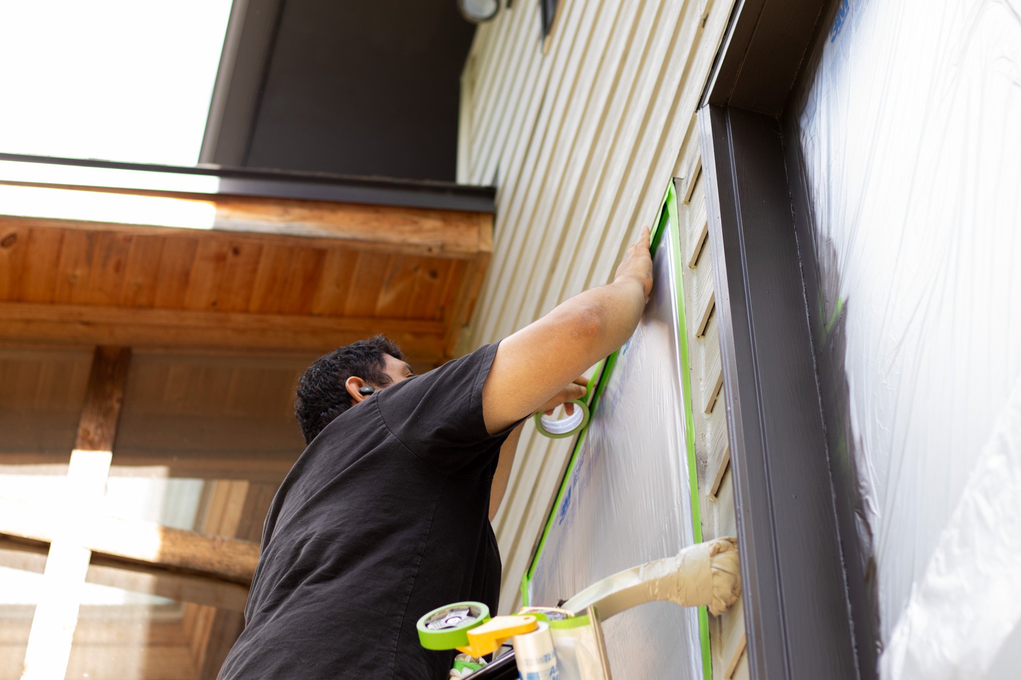 Painter putting up plastic over windows before exterior home painting in Bennington, Nebraska.