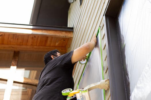 Brush & Roll Painting employee taping off windows of exterior of home before painting.