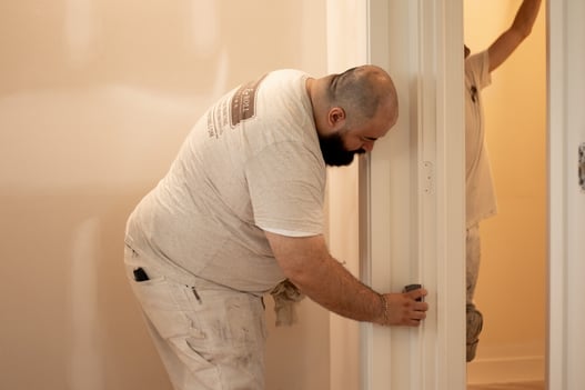 Painter sanding a wood doorframe before repainting it white.