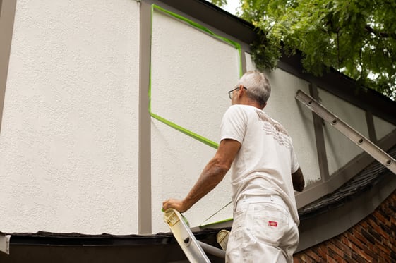 Brush & Roll Painting painter peeling tape off of exterior of home after painting it white.