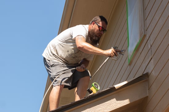 Painter spraying exterior of house a warm beige color in Omaha, NE.