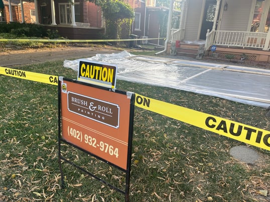 Brush & Roll Painting yard sign outside of a Omaha home with lead exterior paint and caution tape around the yard.