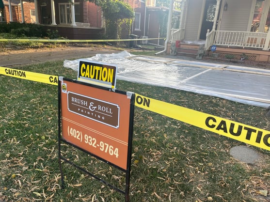 brush & Roll Painting yard sign with caution tape around a house being painted and scraped with lead paint.