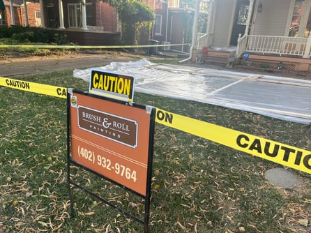 Brush & Roll Painting sign in front yard of home with caution tape for lead paint safety.