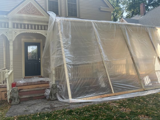 Exterior of house with large plastic and wooden structure covering the porch for lead paint remediation.