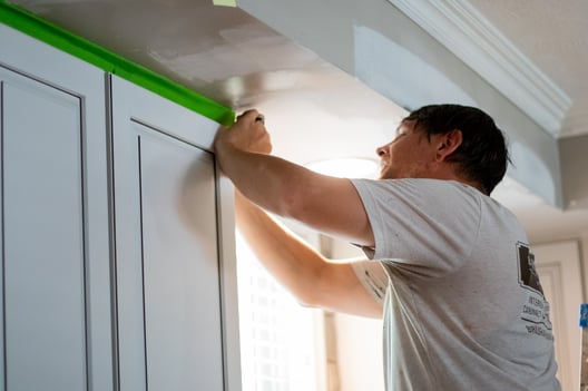 Painter taping off cabinets to paint kitchen walls in Omaha, NE.