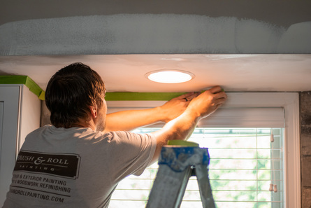 Painter taping off kitchen window before painting ceiling and walls in Council Bluffs, NE.