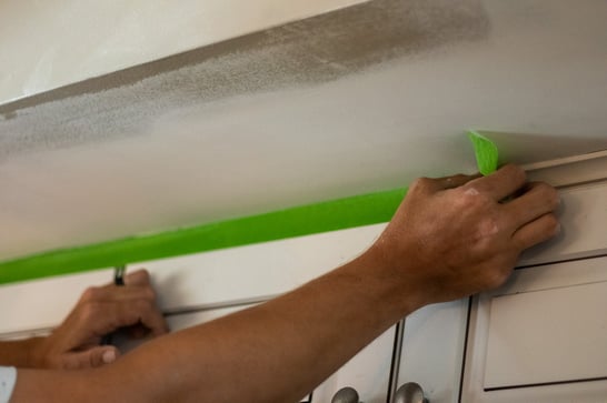 Painter putting up tape on cabinets before painting walls and a ceiling.
