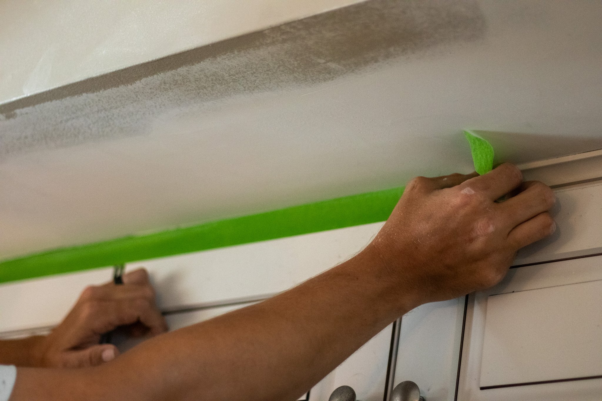 Painter placing green frog tape on cabinets before painting the wall above it.