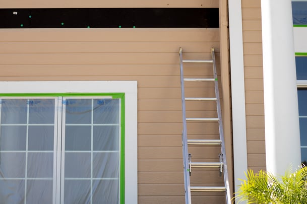 Exterior of house with windows taped and plasticed off with a board missing on the side of the home with a ladder against the wall.
