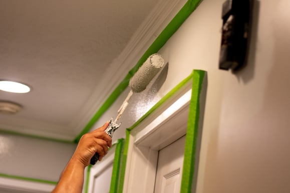 Person rolling white paint on to wall.