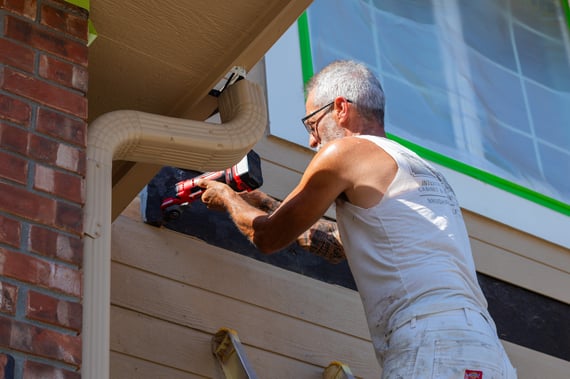 Painter doing a minor siding repair on the exterior of house before painting.