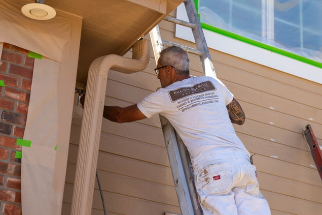 Painter on a ladder on the outside of a house spraying the siding with beige paint in Omaha, Nebraska