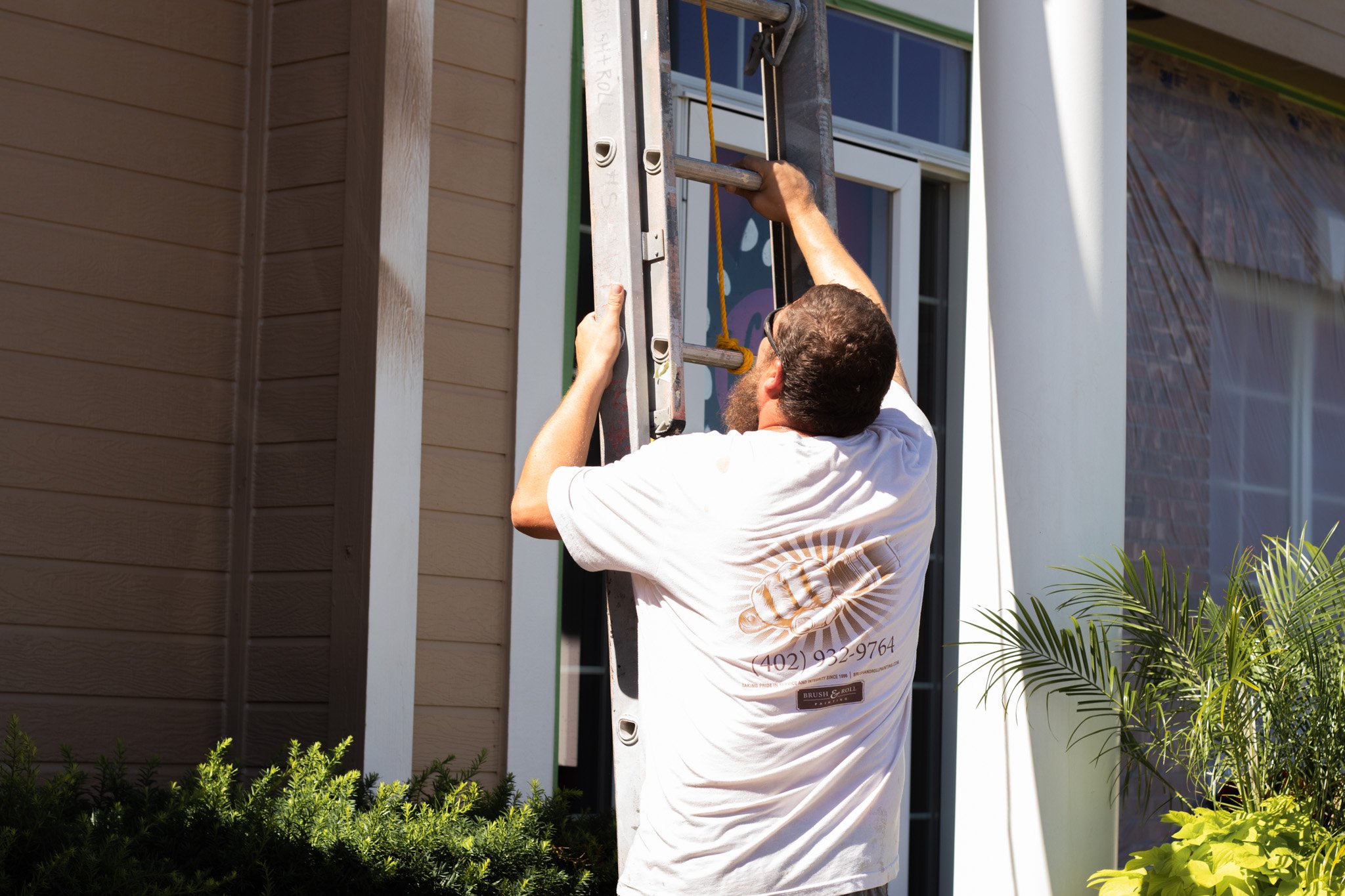 Painter moving a ladder outside of a house exterior being painted in Omaha, NE.
