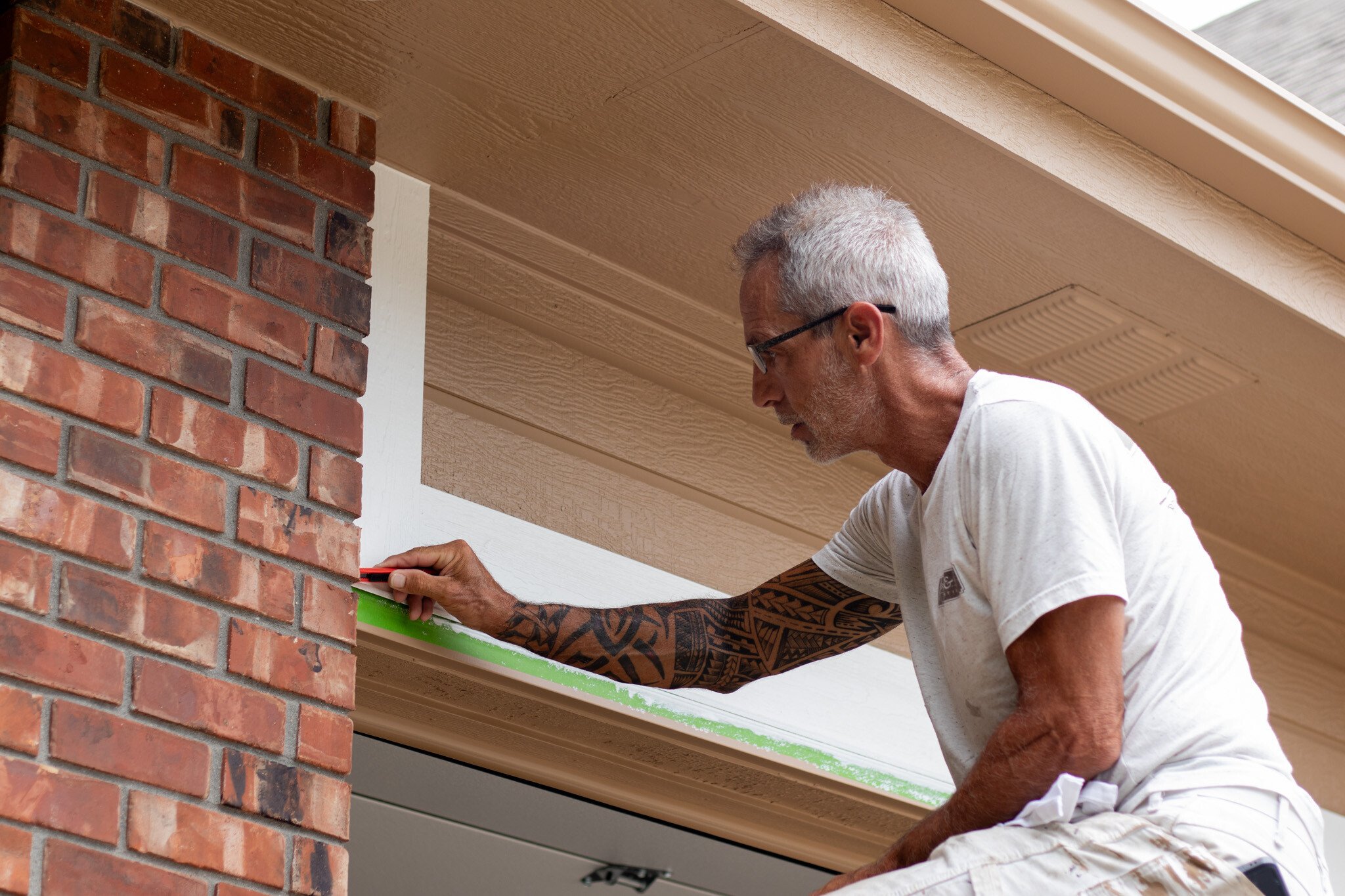 Brush & Roll Painting painter touching up paint above a garage on a home in Omaha, NE.