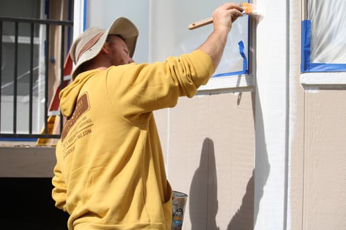 Brush & Roll Painting painter brushing on exterior house primer onto a wood board in Omaha.