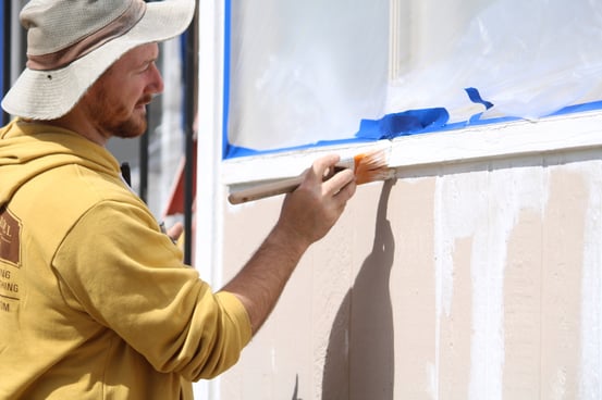 Painter priming exterior of house before painting.