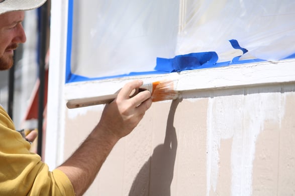 Painter priming window trim with white primer and a brush.