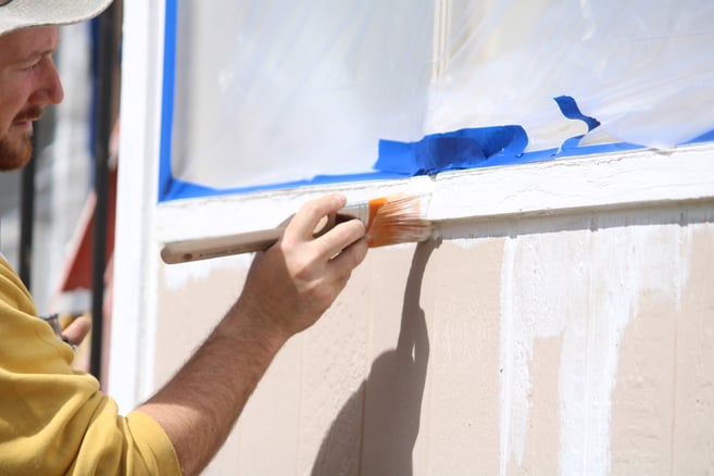 Painter brushing primer onto window trim outside a home.