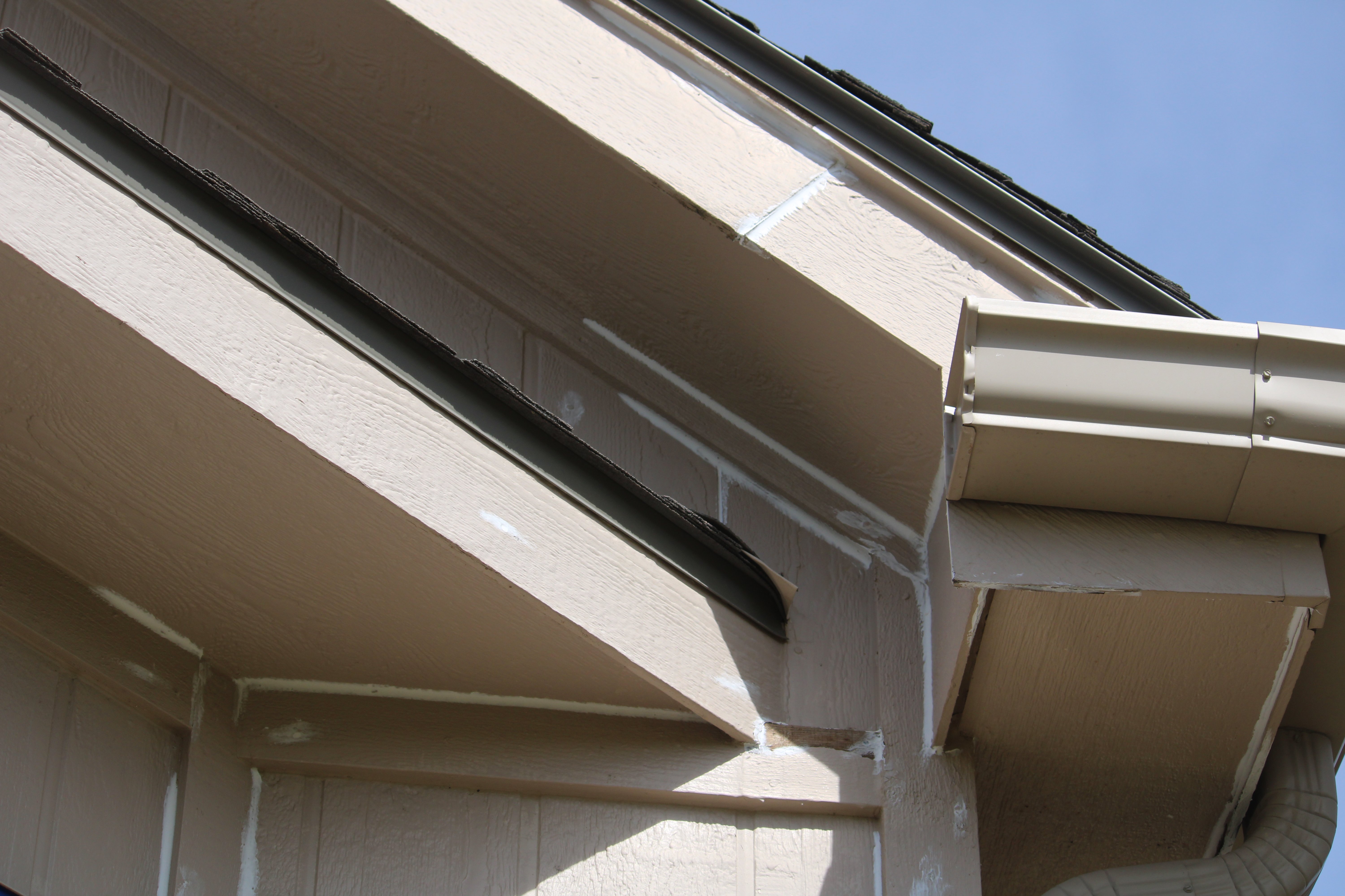 Corner of house with caulk in gaps in the process of being painted by Brush & Roll Painting in Omaha, NE.