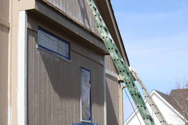 Ladders against an exterior of a house that is being caulked and primed before exterior painting.