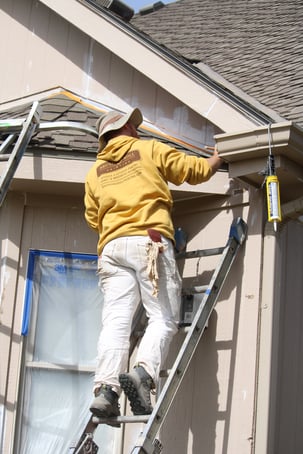 Exterior painter at Brush & Roll Painting on a ladder against the back of a house priming spots before painting.