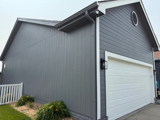 Exterior of house freshly painted a dark grey color with white trim and white garage.