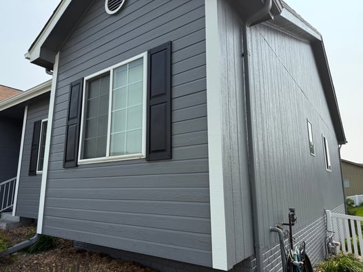 Exterior painted house in Omaha, NE with dark grey siding, navy shutters, and white trim and gutters.
