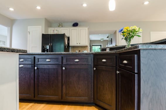 Kitchen island stained a dark brown with handles on drawers and knobs on doors.