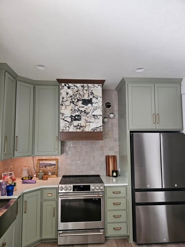 Kitchen oven area with light sage green cabinets and marble oven top with a dark brown stain on the oven hood.