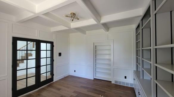 Interior home office space with walls and ceiling painted white with black trim around glass door frame and bookshelf painted light grey.