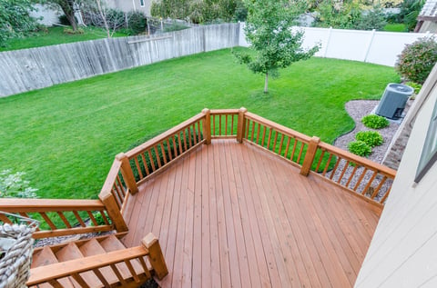 Upper view of wooden deck stained a medium warm brown color and yard with green grass.