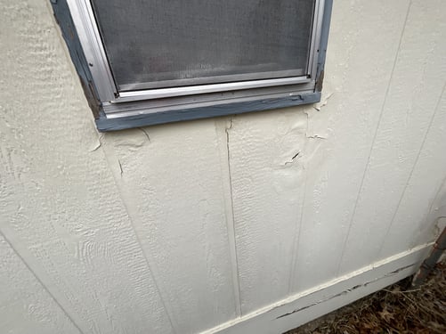 Exterior siding of home next to a window with cracking boards and wood.