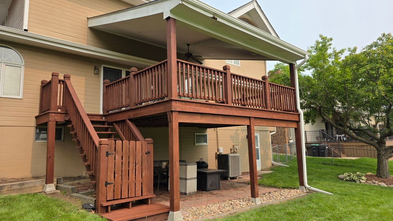 Back wood deck stained a dark brown color with a gate at the bottom of the stairs outside of a home in omaha, NE.