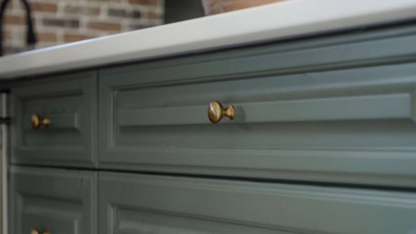 Sage green cabinet drawers with gold knobs and white countertop.