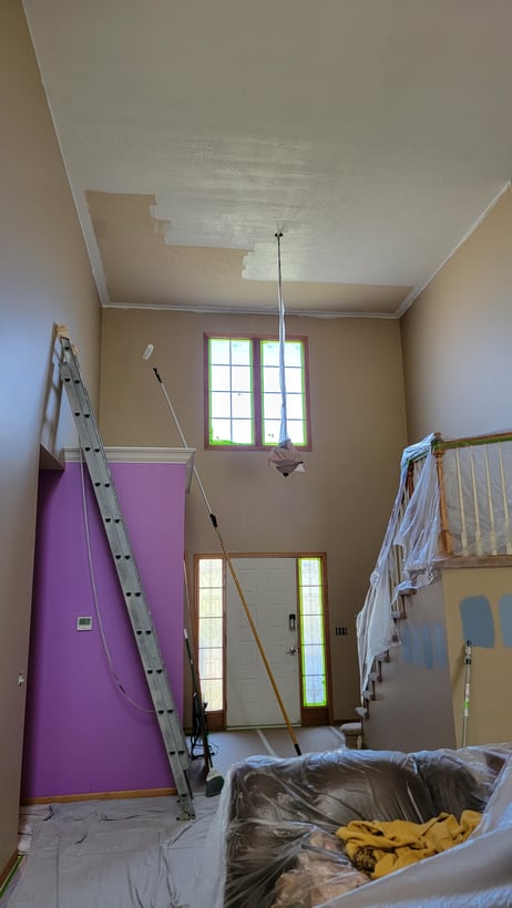 Entryway with painting supplies around and white paint being rolled onto the ceiling.