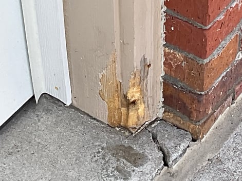 Damaged light brown siding around garage door of brick home.