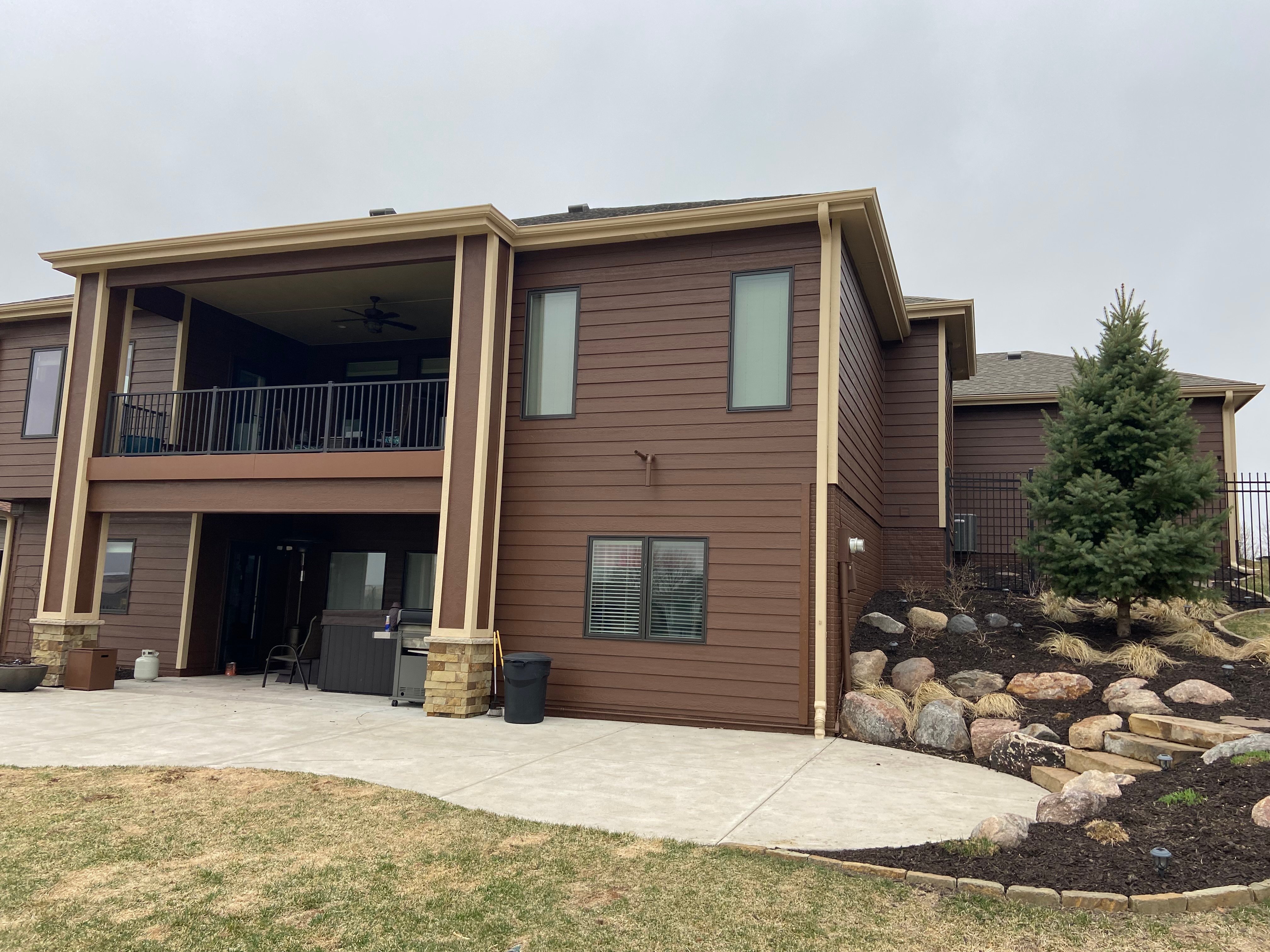 Backside of a house with exterior that has been painted a dark brown with a redish tone. The windows have dark black trim and the down spouts are beige. The home is in Omaha, NE painted by Brush & Roll Painting.