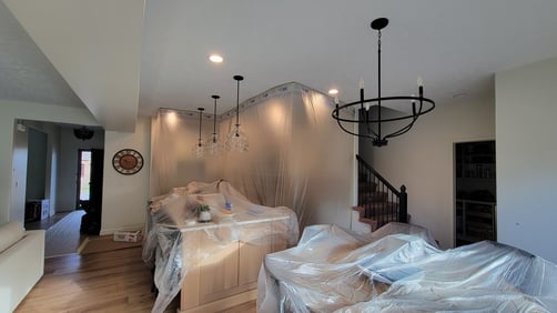 Furniture and cabinets in a kitchen covered with plastic and tape to protect it from paint on ceiling.