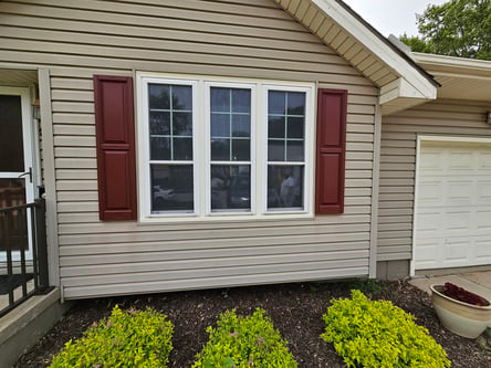 Exterior siding of house painted a light beige color with dark red shutters and white window trim and garage door.