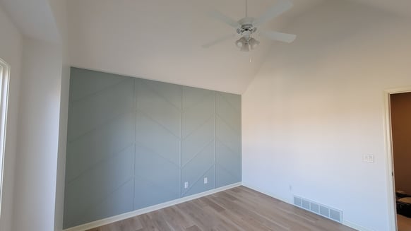 Interior of a home living room with a sage green accent wall with wood detailing and white walls and ceiling.