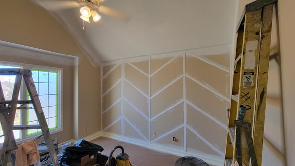 Interior room in the process of being painted white with a sage green accent wall and wood detailing.