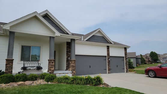 Exterior of a home painted white with gray garage doors and pillars with brown stone brick.