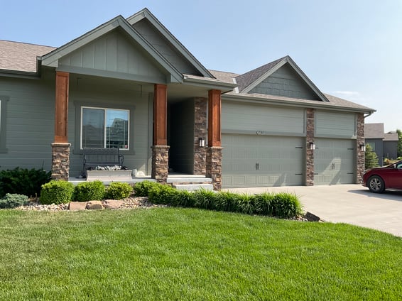 House painted sage green with wood pillars and stone accents.