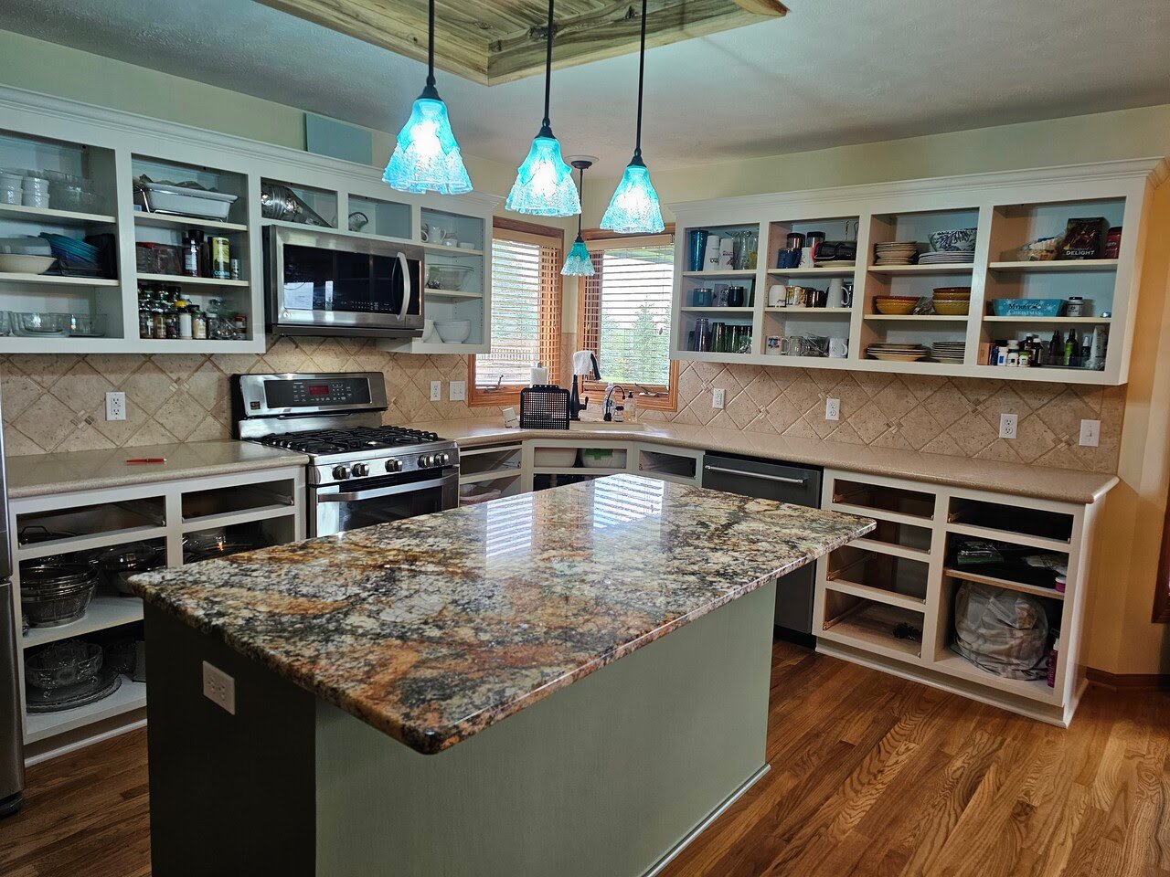 Cabinet doors and drawers removed in a kitchen for painting. The wall cabinets are painted white and the island is painted sage green.