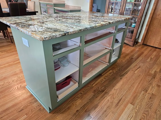 Kitchen island painted a dark sage green with granite countertops and the doors removed for painting.