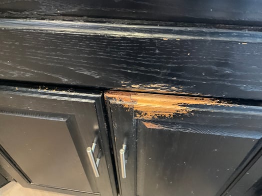 Kitchen cabinets with peeling and chipping black paint on top and silver handles.