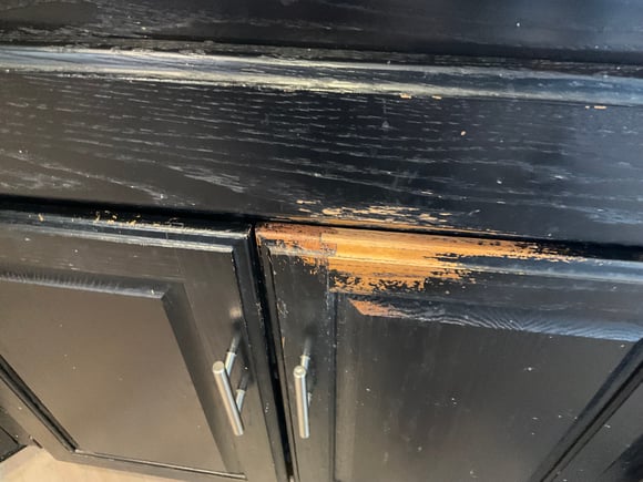 Cabinet doors painted black with paint chipping off, revealing golden oak wood.