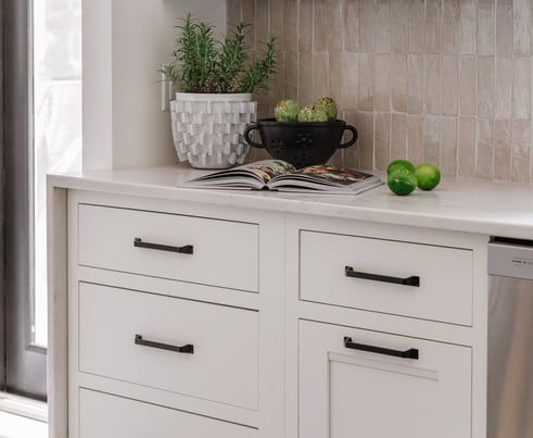 Kitchen with white painted cabinets with long black handles and white countertops.